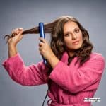 lady in pink robe using a flat iron but what is a hair straightener?
